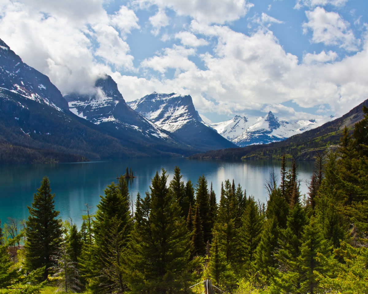 Scenic lake nestled among towering mountains and lush trees.